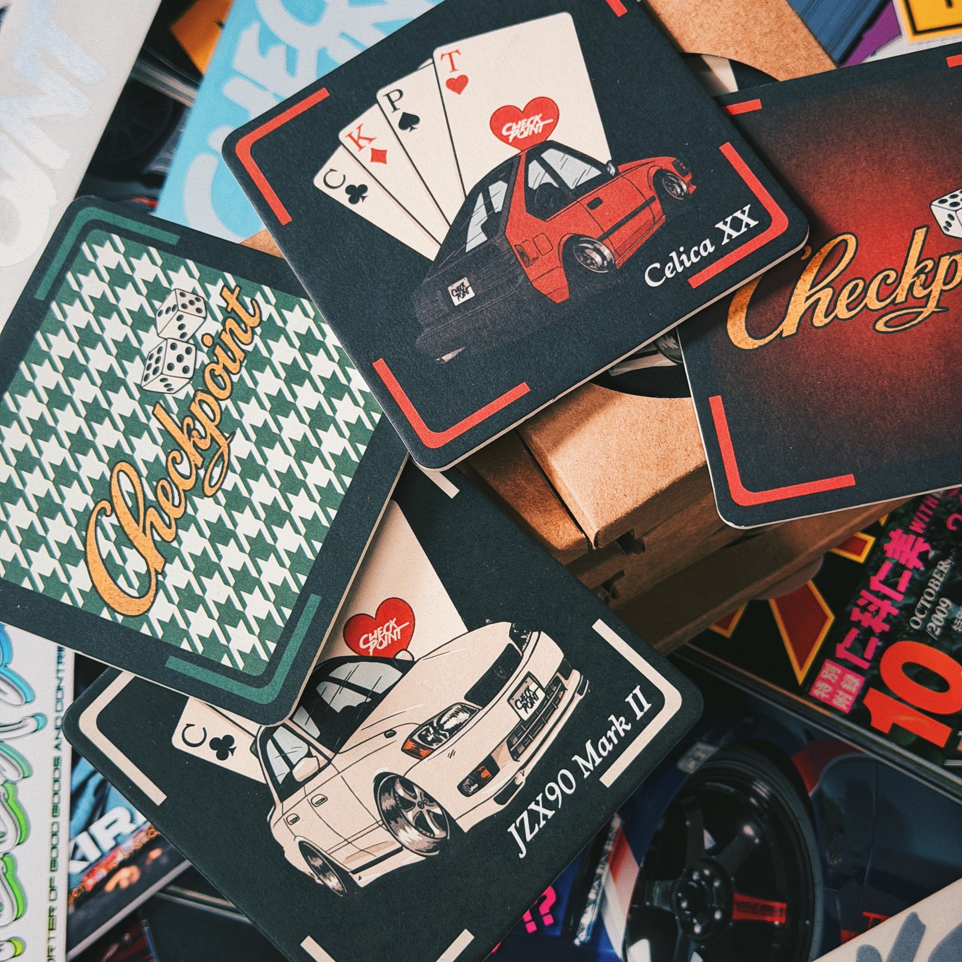 A pile of Japanese-style playing cards featuring car illustrations and the word 'Checkpoint' in multiple colorways, arranged on top of a cardboard box.