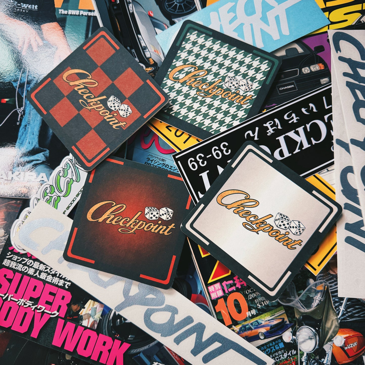 A pile of various Checkpoint brand stickers and decals with different designs, including checkered patterns, text decals, and a houndstooth pattern, displayed on top of other magazine pages.